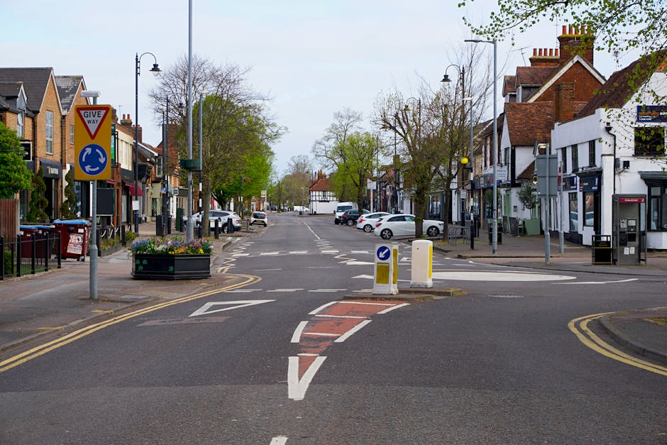 A quiet residential street in Reigate with a no-through road sign on the left, surrounded by shops and houses with brick and white facades. The pavement features parked cars, street lamps, and a large