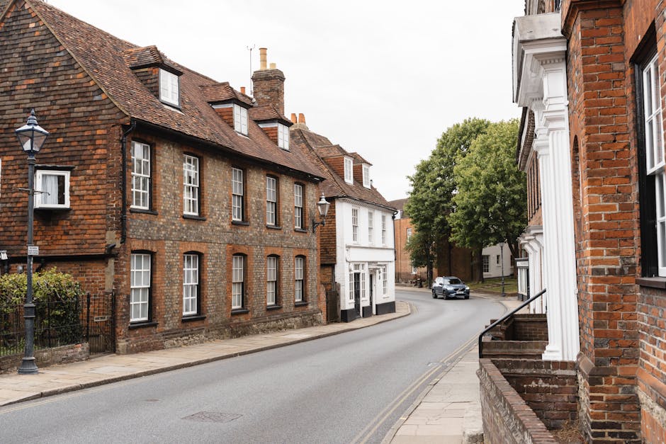 A quiet residential street in Reigate with a no-through road sign on the left, surrounded by shops and houses with brick and white facades. The pavement features parked cars, street lamps, and a large