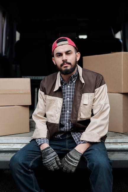 Two movers from Movers Surrey are engaged in a home relocation process outside a residential property, transferring cardboard boxes and furniture from the driveway into a white panel van. One mover is